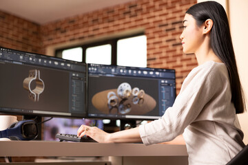 Focused female remote worker designing metal components using CAD software on desktop monitors. Industrial product asian developer analyzing 3D models on computer in brick wall home.