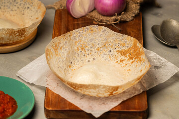 Close-up view of a freshly made Sri Lankan hopper (appa) with crispy edges and soft center, presented on parchment paper with ingredients like onions and chili paste. Perfect for Sri Lankan cuisine