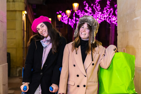 Two smiling women carrying shopping bags and crutches at christmas market