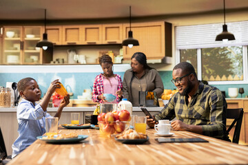 Father working on his smartphone and serving breakfast with his cute family, gathered in the kitchen to enjoy the simple comfort of morning togetherness. Happy start to the day with sunlight.