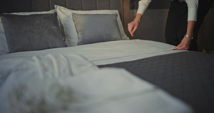 Chambermaid Smoothing Bed Sheets and Aligning Decorative Pillows in Stylish Modern Hotel Bedroom. Concept Professional Housekeeping, Guest Room Maintenance, Comfort focused Accommodation Service.
