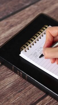 Hand is writing inspirational Christian text to trust God and Jesus Christ in a notebook with holy bible book. Vertical video. Biblical concept.