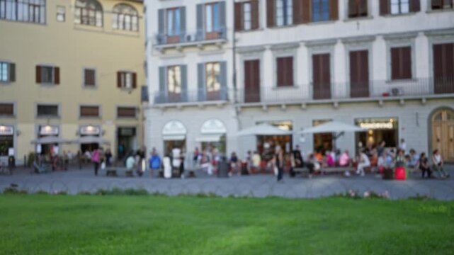 Defocused city street with soft bokeh lawn foreground and blurred cafe facades; background backplate copyspace calm.