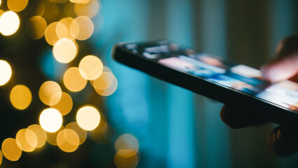 Hand flips through photos on a smartphone at night in front of a Christmas tree