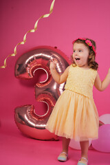 Young girl celebrating third birthday with pink balloons