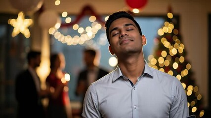 Peaceful young South Asian man with eyes closed, meditating or relaxing at a festive holiday party with blurred lights and Christmas tree in the background