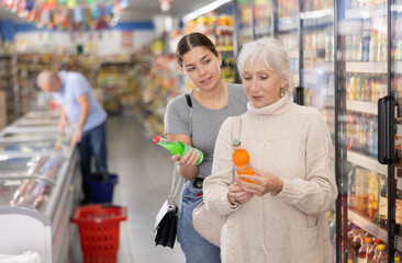 Attentive woman purchasers choosing cool drink out of large stock in a big supermarket