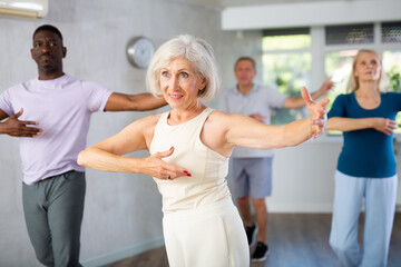 Elderly woman is engaged in dance lesson and repeats basic movements for pair ballroom dancing....