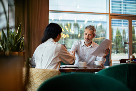 Adult man and woman shaking hands in friendly modern cafe meeting