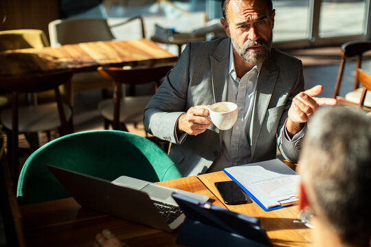 Mature businessman discussing project over coffee in cafe, concerned