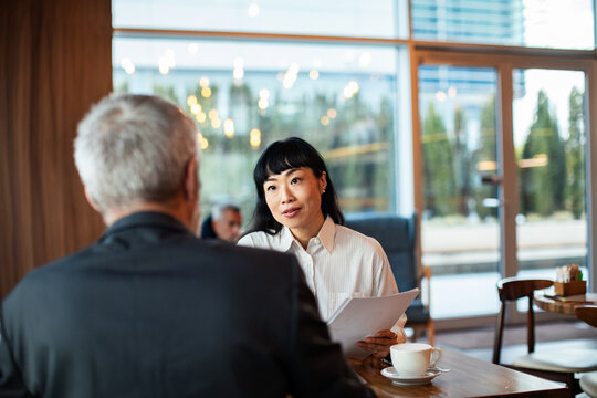 Adult woman consulting senior man at cafe during focused meeting
