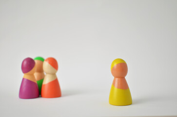 Wooden figure standing alone, separated from other colorful figures, representing exclusion