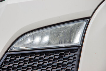 Close-up view of a car headlight with water droplets on the surface, showcasing intricate design details and modern automotive technology in a sleek vehicle exterior