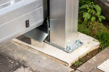 Metal support structure of a modern gate, showcasing detailed craftsmanship and sturdy design, positioned on a concrete base with greenery in the background
