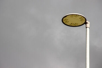 Streetlight with circular yellow lamp against a cloudy gray sky, illuminating the urban environment, showcasing modern design and functionality in public spaces