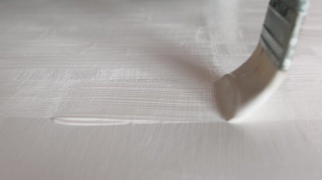 Close up of an artist priming canvas with white ground, preparation for painting. Selective focus