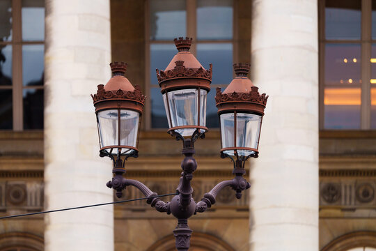 Street lamp with ornate ironwork in front of grand building with stone columns, classic European urban architecture style, decorative and vintage city scene emphasizing historic character of the area