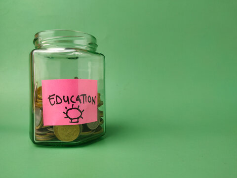 The image shows a glass jar filled with coins, with a pink sticky note on it that says EDUCATION