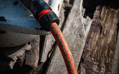 Close-up of an orange garden hose with a black and red connector attached to a white metal faucet....