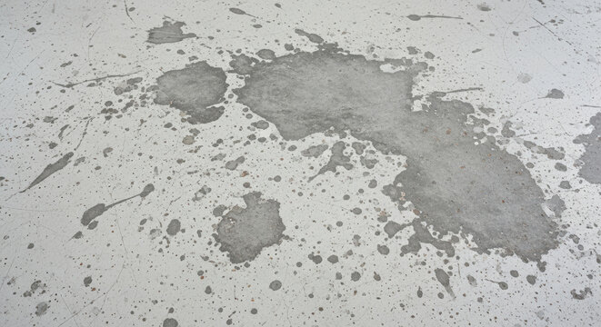 Large gray splotch and scattered stains on worn white concrete floor, abstract pattern from paint splashes, smudges, and irregular surface texture details