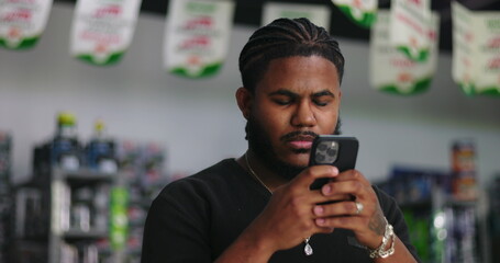 Young man of African descent intently focused on smartphone screen in a store environment, illustrating digital engagement and modern reliance on technology