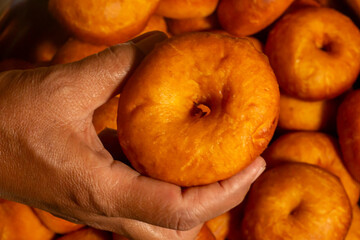 holding a donut with stack of fried donuts as the background