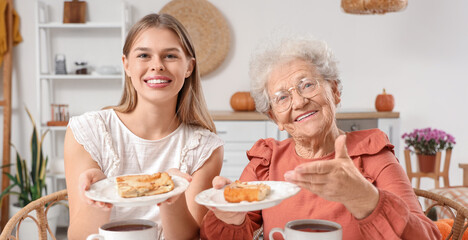 Young woman and her grandmother with pieces of apple pie at table in kitchen