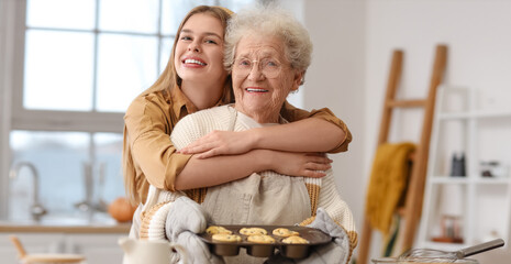 Young woman hugging her grandmother with muffins in kitchen