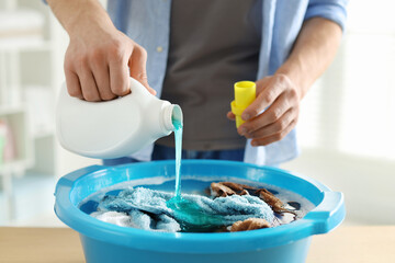 Man pouring detergent into plastic basin with towels at table indoors, closeup