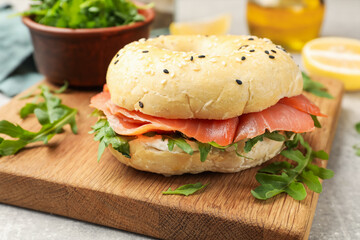 Delicious bagel with salmon and arugula on grey table, closeup