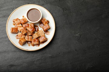 Tasty candies with salt and caramel sauce on dark textured table, top view. Space for text