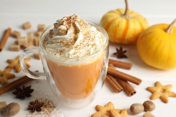 Tasty pumpkin latte with whipped cream in glass cup, cookies and ingredients on white wooden table, closeup
