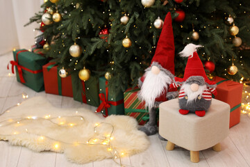 Naklejka premium Funny gnomes near Christmas tree and gift boxes in decorated room, space for text