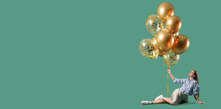 Beautiful young woman with air balloons sitting on green background