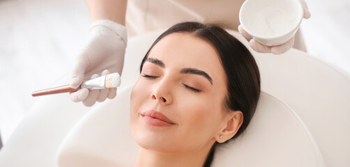 Cosmetologist applying mask on woman's face in beauty salon