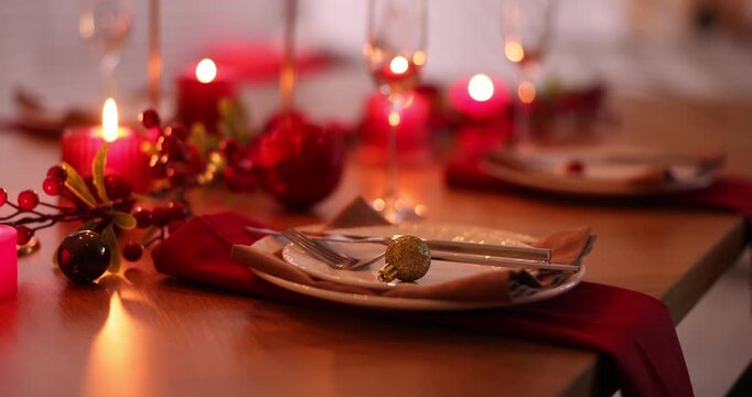 Stylish Christmas table setting with plates, glasses and burning candles in festive decorated room, closeup. Camera moving in