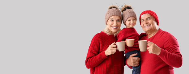 Fototapeta premium Cute little boy with happy grandparents in warm sweaters with cups of tea on grey background