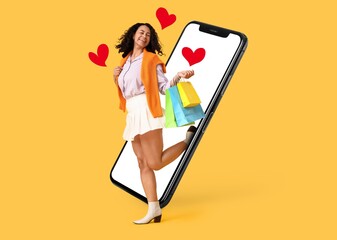 Happy female blogger with shopping bags and big mobile phone on yellow background