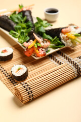 Plate with tasty sushi cones, rolls, lambs lettuce and bamboo mat on color background, closeup