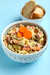 Bowl of tasty Olivier salad on blue background