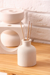 Bottle of reed diffuser and decor on table near light brick wall in room, closeup