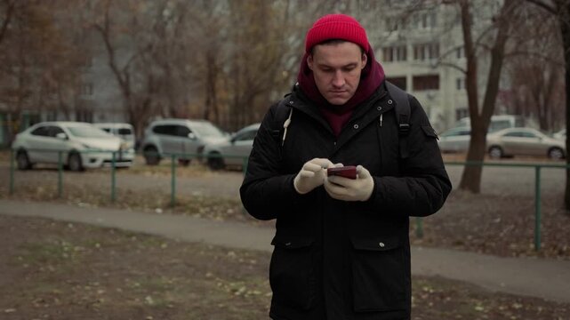 Man in winter attire checks smartphone outdoors in a park during autumn - Powered by Adobe