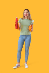 Young woman with bottle of detergent and toilet brush on orange background