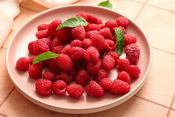 Plate with fresh raspberries and mint on pink tile background