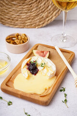 Wooden board of tasty baked Camembert cheese on light background