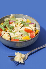 Bowl of tasty pasta salad with pepper and red onion on blue background