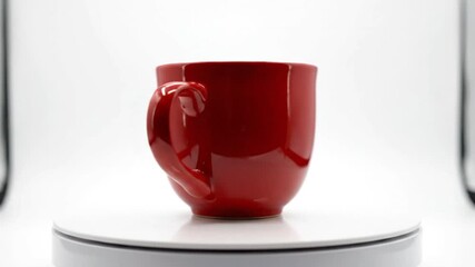 A shiny red cup sits on a white saucer against a clean white background, celebrating Red Cup Day with a simple composition.