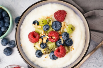 Bowl of tasty semolina porridge with fresh berries and kiwi on white background