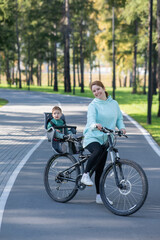 Obraz premium Caucasian woman rides bicycle with one-year-old son in park. Vertical photo. 