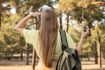 Female traveler with compass and backpack in forest, back view